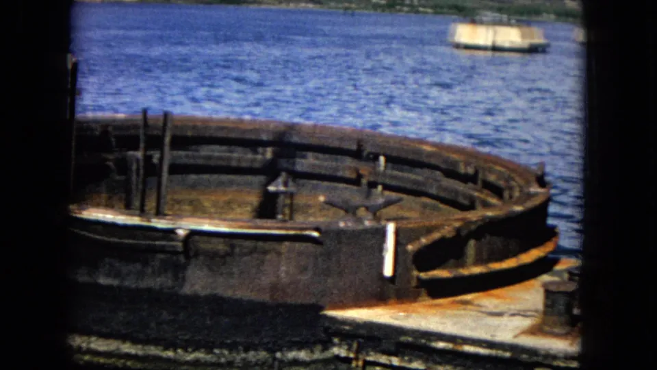 1968 Honolulu 8mm frame showing a rusted circular gun turret foundation on a dock beside blue harbor water.