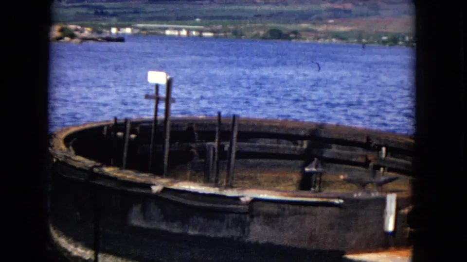 Honolulu waterfront frame with a weathered circular foundation, upright posts, and a small sign near blue harbor water.