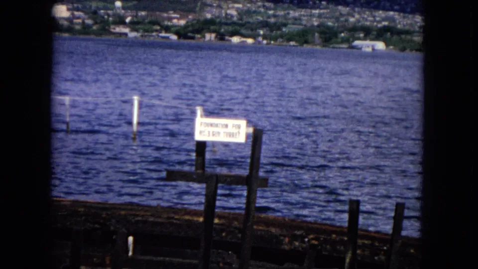 1968 Honolulu frame centered on a sign for the No. 3 gun turret foundation, with blue water and shoreline behind it.