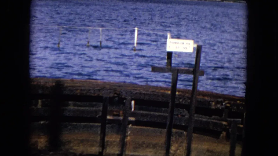 Honolulu 8mm frame showing the gun turret foundation sign over rusted dock metal and blue harbor water.