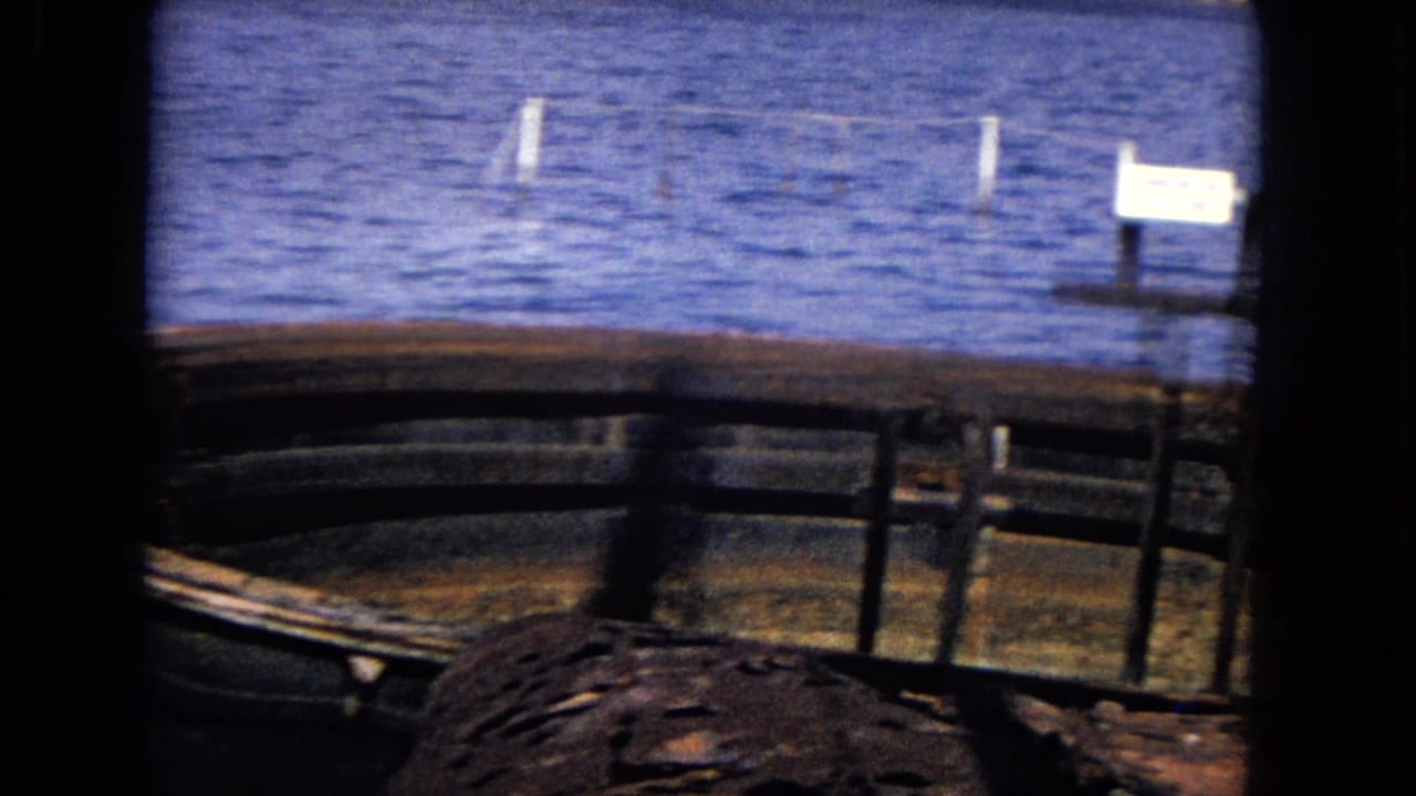 Rusted curved ship remains sit in blue water with a small white sign in the background.