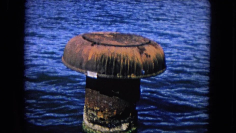 1968 Honolulu footage centers on a corroded cylindrical buoy or piling, its rusted top and stained base surrounded by blue harbor water.