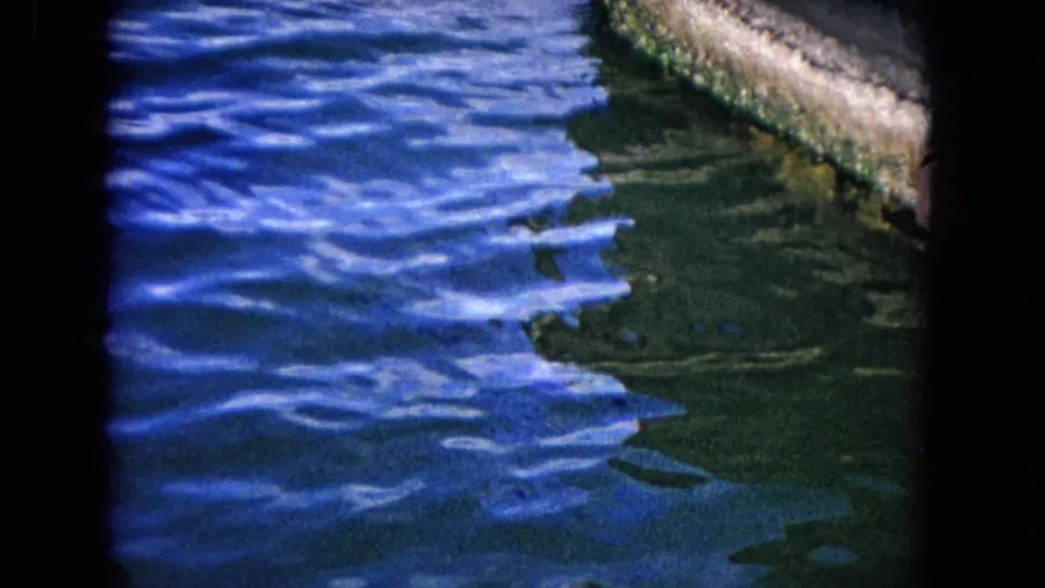 1968 Honolulu home-movie frame focused on rippling blue-green water beside a hard waterfront edge.