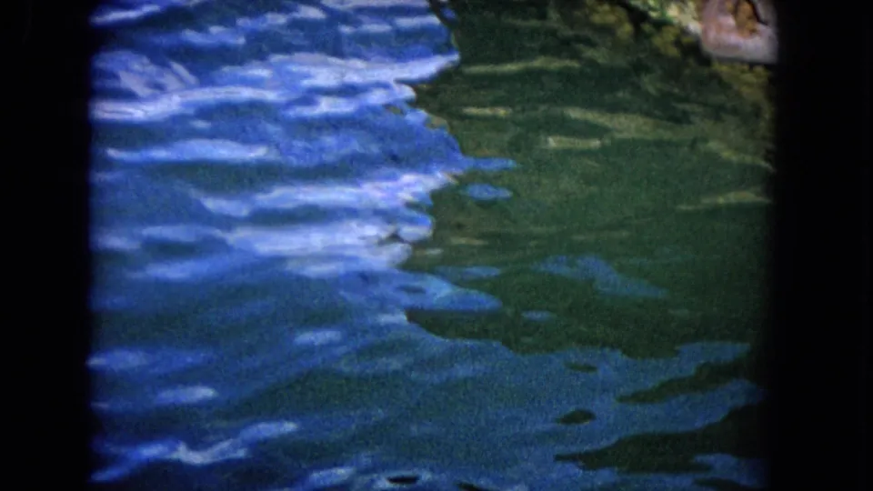 1968 Honolulu 8mm frame showing textured harbor water with blue highlights and a partial waterfront edge.