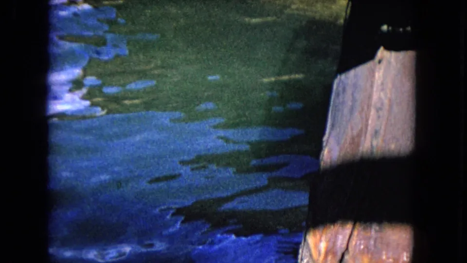 1968 Honolulu home-movie frame with rippling harbor water and a weathered post partly visible along the right edge.