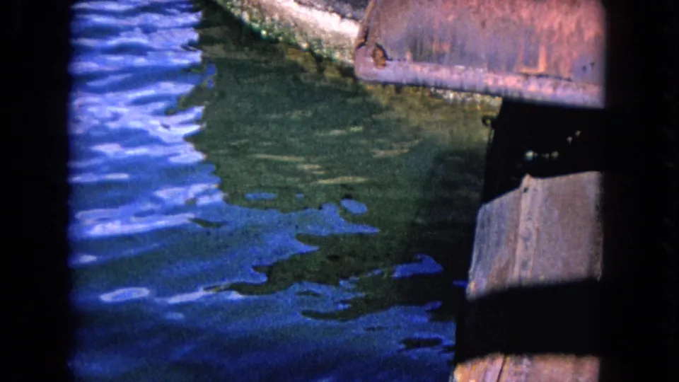 Close 8mm view of Honolulu dock timbers and blue-green water, framed by dark pier supports.