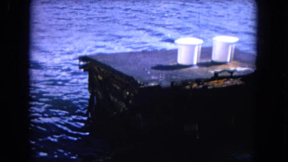 Two white cups sit on a dark dock corner above blue water in the 1968 Honolulu home-movie footage.