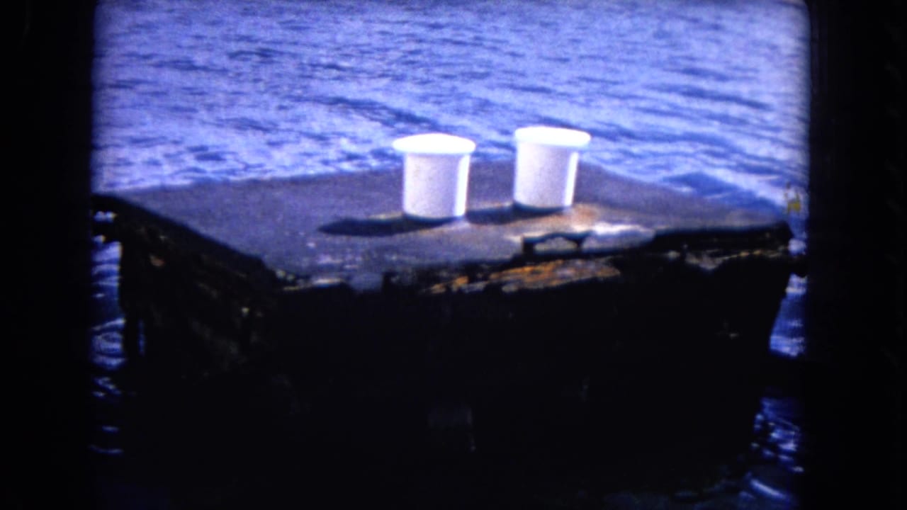 Weathered concrete pier with two white bollards above blue ocean water.
