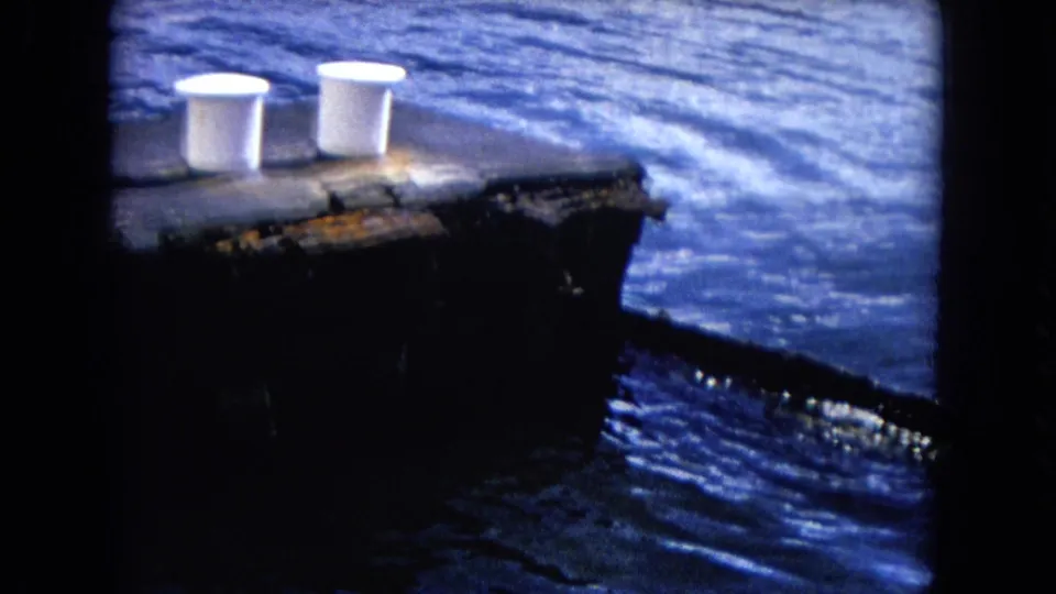1968 Honolulu home-movie frame with two white bollards on a weathered pier and rippled blue water behind it.
