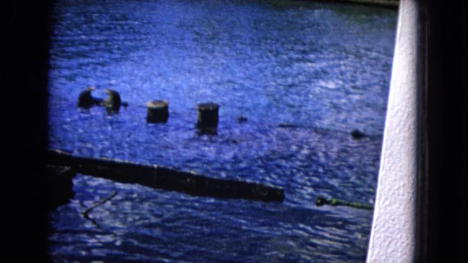 1968 Honolulu 8mm frame looking across blue ocean water toward small dark posts and a low pier edge.