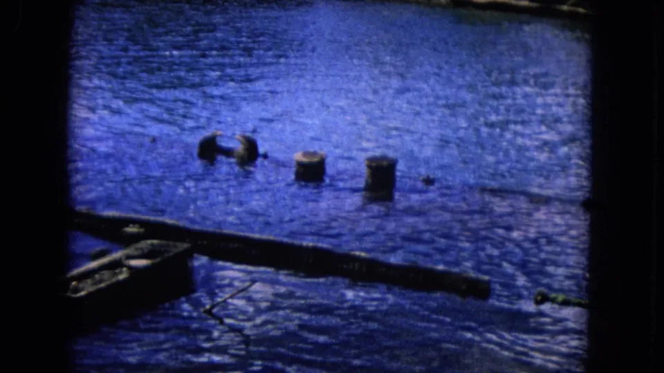 1968 Honolulu home-movie frame showing rippling blue water, dark posts, and a low waterfront structure at the bottom edge.