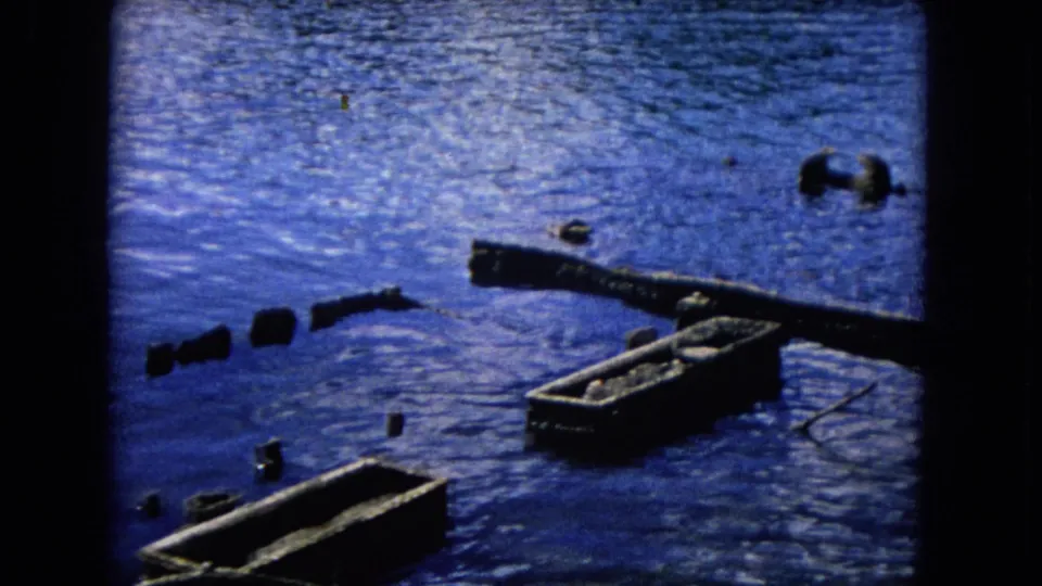 1968 Honolulu waterfront view with broken dock pieces, scattered pilings, and an empty hull in rippled blue water.