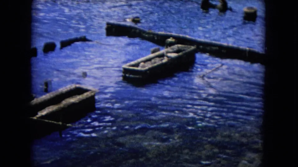 1968 Honolulu 8mm frame with empty hulls, a weathered crossbeam, scattered posts, and saturated blue harbor water.