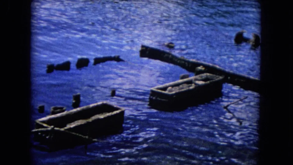 1968 Honolulu waterfront view with two small wooden raft-like forms, scattered debris, rippled water, and dark film borders.