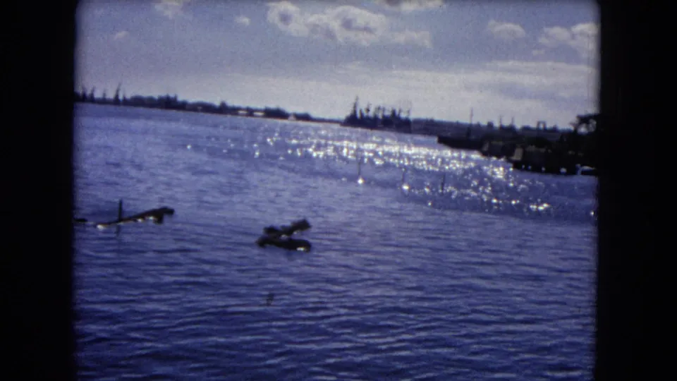 1968 Honolulu water view with bright glare, floating logs or debris, distant shoreline silhouettes, and a partly cloudy sky.