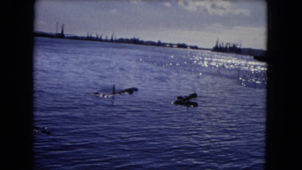 1968 Honolulu home-movie frame showing open water, floating debris, shoreline structures, bright sky, and 8mm frame edges.