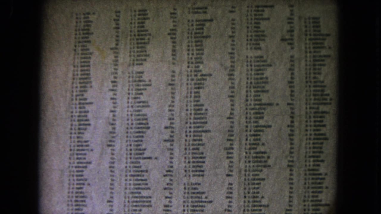 Columns of names on a memorial wall seen in soft, grainy 8mm footage.