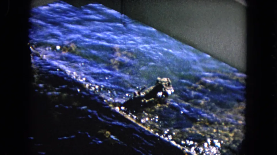 1968 Honolulu 8mm frame with blue harbor water, dark shoreline or structure edge, and bright reflected highlights.