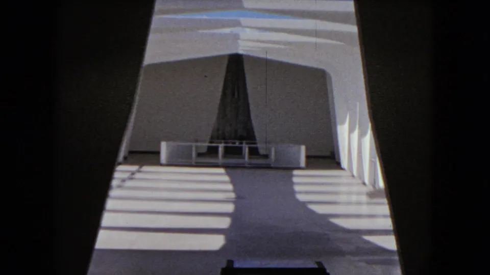 1968 Honolulu frame looking through a shadowed opening toward a dark vertical structure and bands of sun on a pale floor.
