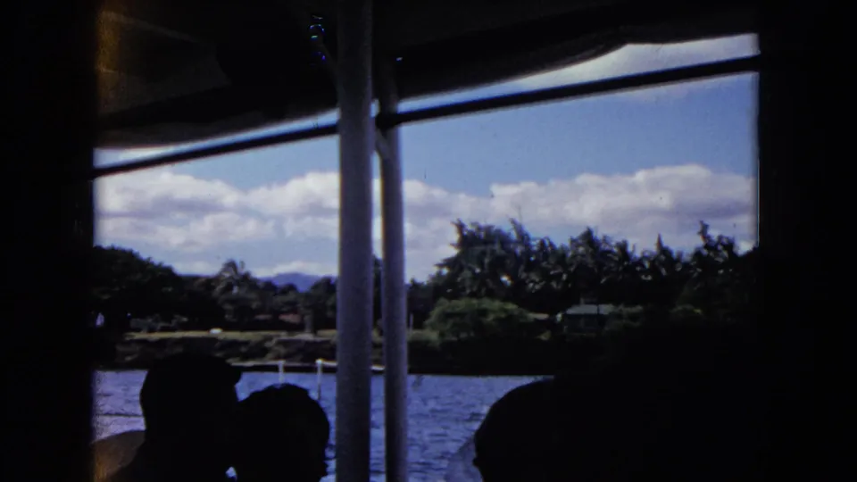 Honolulu boat-ride view with silhouetted riders in the foreground and a green shoreline across the water.