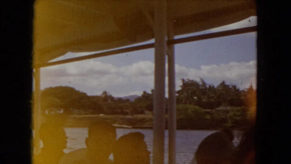 Warm 8mm frame from a Honolulu boat interior, with passenger silhouettes against water and tropical shoreline.