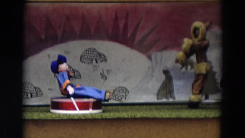 Toy stage scene from the 1968 Lahaina Maui home movie with a blue-suited puppet and fur-parka puppet before painted igloos.