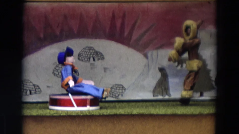 1968 Lahaina Maui 8mm frame showing a blue-suited puppet seated on a stage opposite a fur-parka puppet in an Arctic scene.