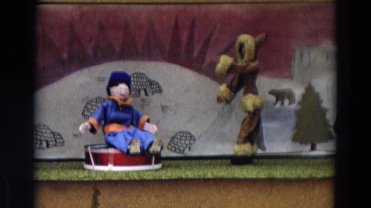Blue-and-orange puppet seated on a red sled beside a fur-trimmed figure on a painted Arctic stage.