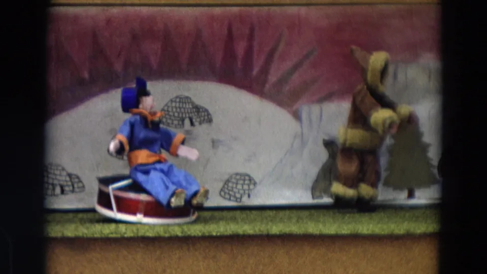 The final frame shows the blue-and-orange puppet turned in profile on the red sled as the larger figure moves near the backdrop tree.