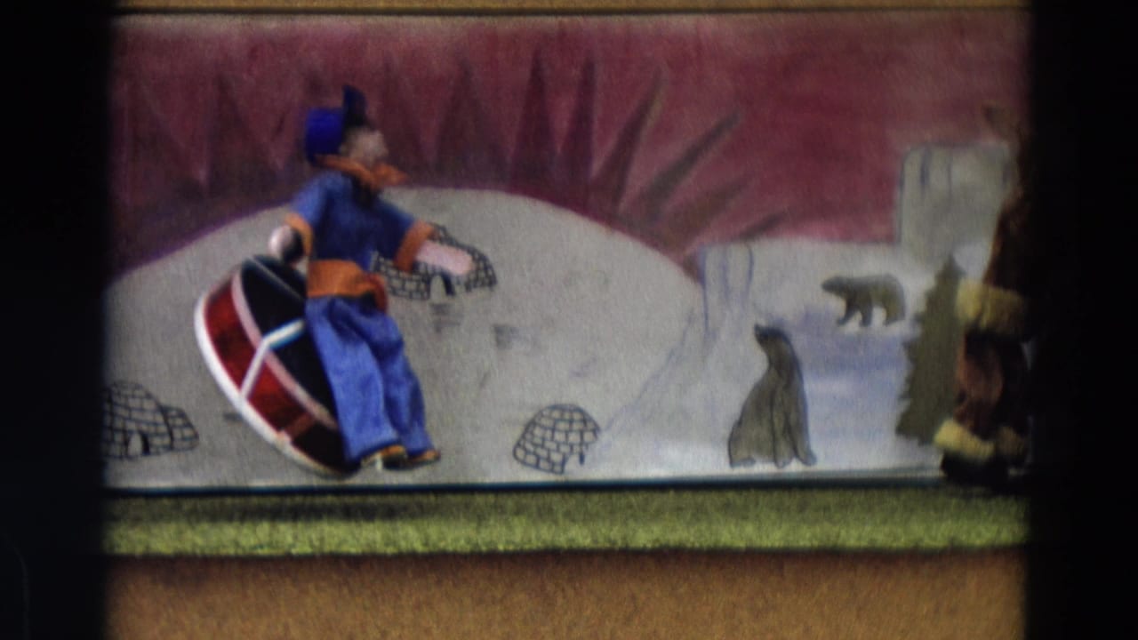 Puppet in blue and orange rides a red-and-white sled across a painted snowy stage.