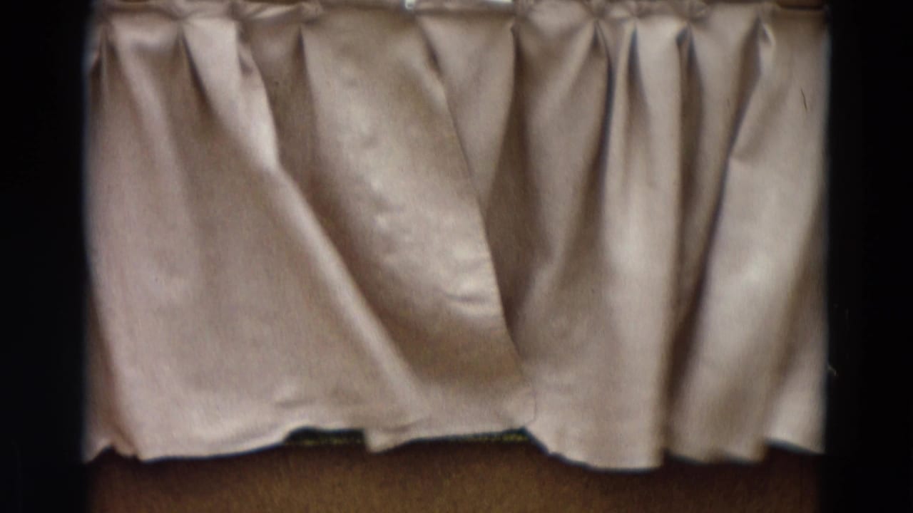 Closed light fabric curtain above a small stage floor, framed by dark film edges.