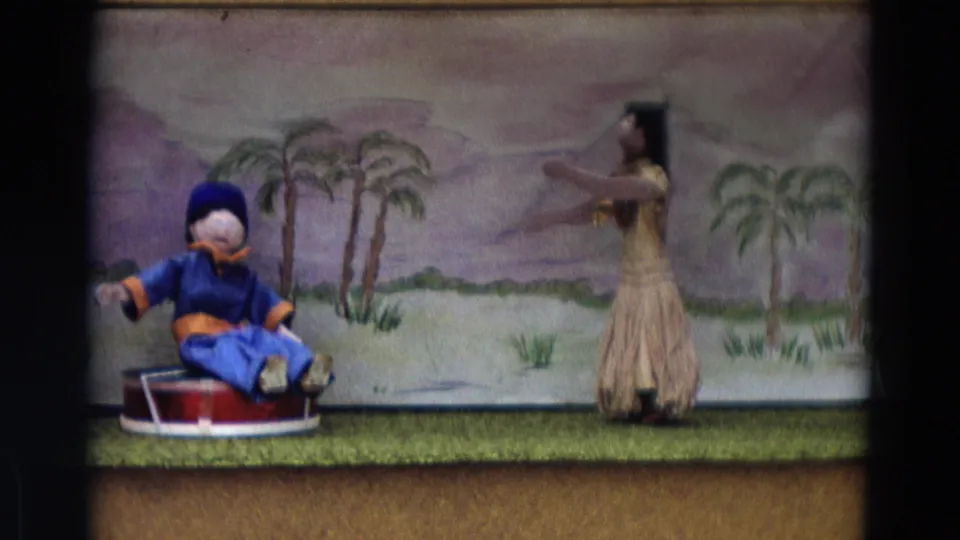 Home-movie frame from the 1968 Lahaina Maui reel showing a puppet and skirted dancer figure on a painted stage set.