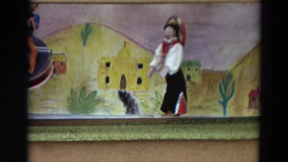 1968 Lahaina, Maui 8mm frame of a female puppet beside a small animal figure before a painted desert village scene.