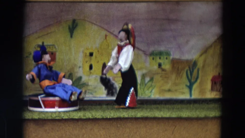 1968 Lahaina Maui home-movie frame of a puppet-show tableau with a blue seated figure and a standing costumed figure on a small stage.