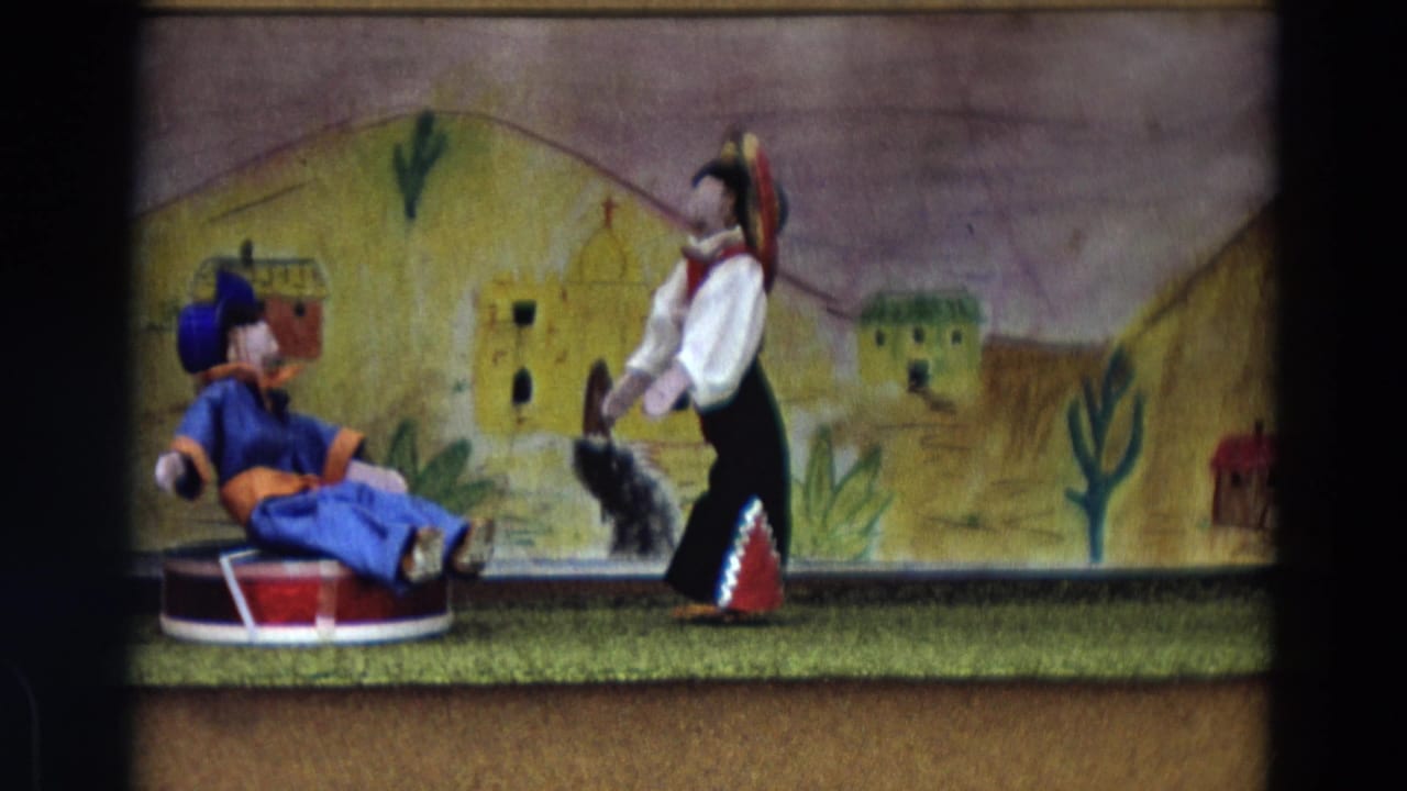 Two puppets perform before a painted Mexican village backdrop with cacti.