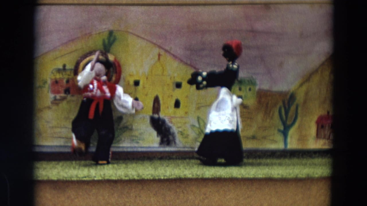 Two costumed puppet dolls face each other on a small stage with a painted backdrop.