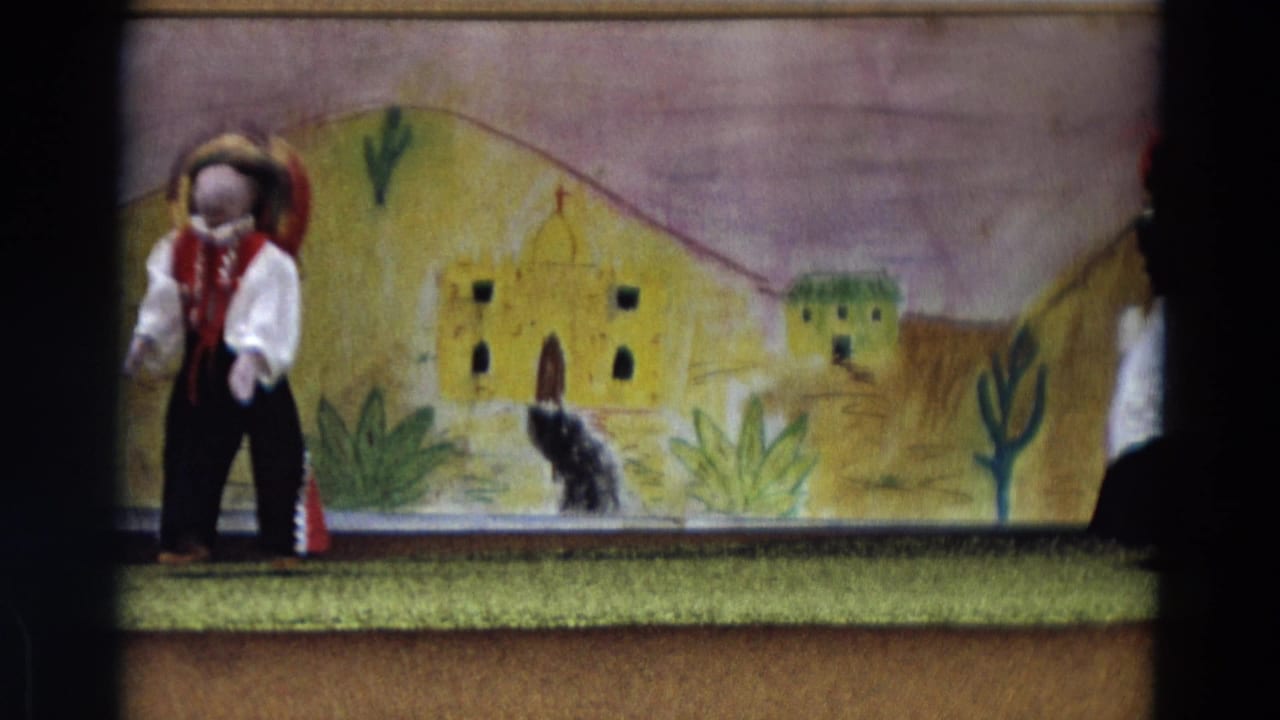 1968 8mm frame with one puppet at left and a small black dog figure near the painted village scenery.