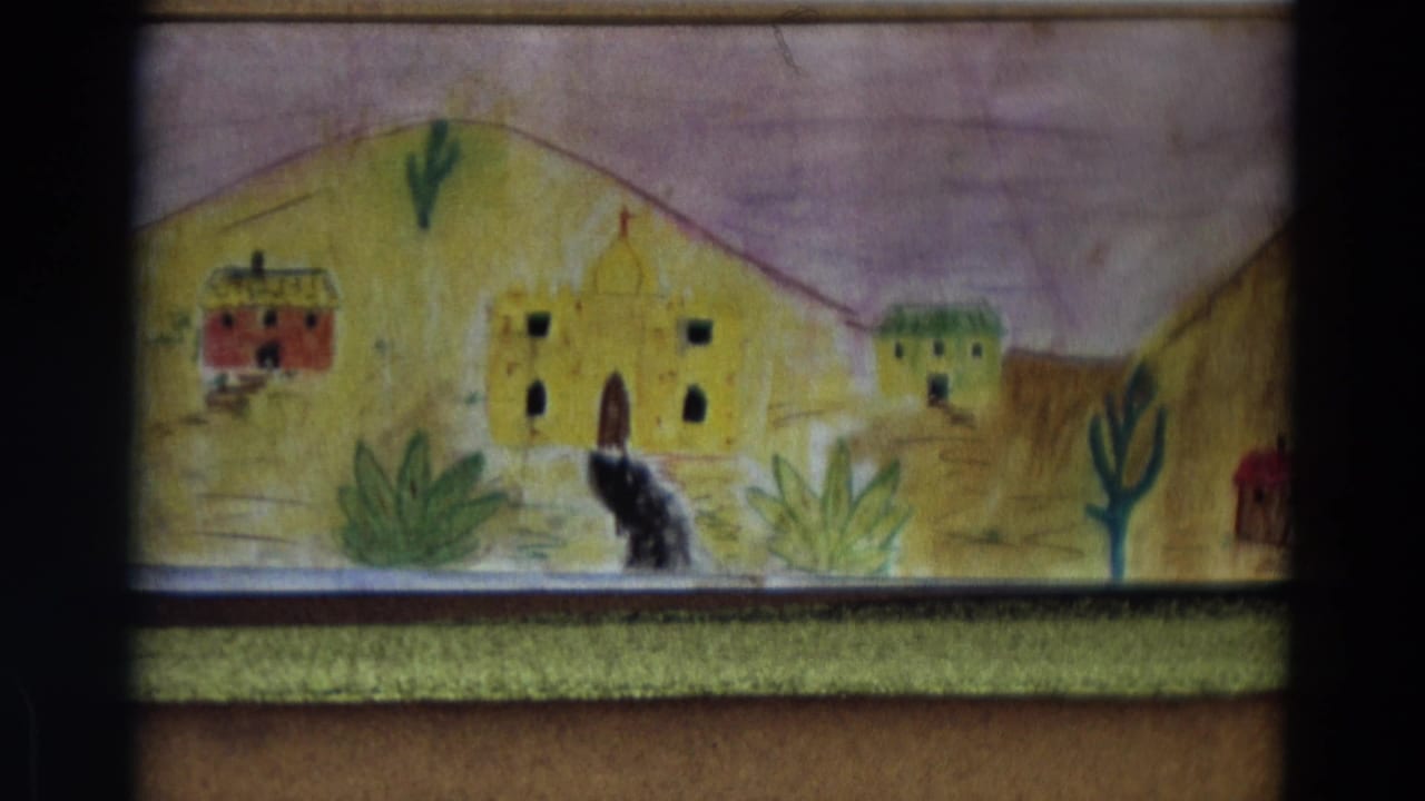 1968 Lahaina, Maui home-movie frame showing a handmade village backdrop with small buildings, desert plants, hills, and a dark figure in front.