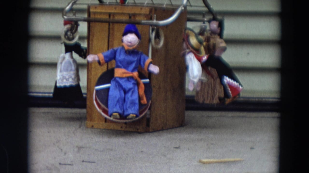 Static view of a central blue puppet and several string puppets on a wooden display.