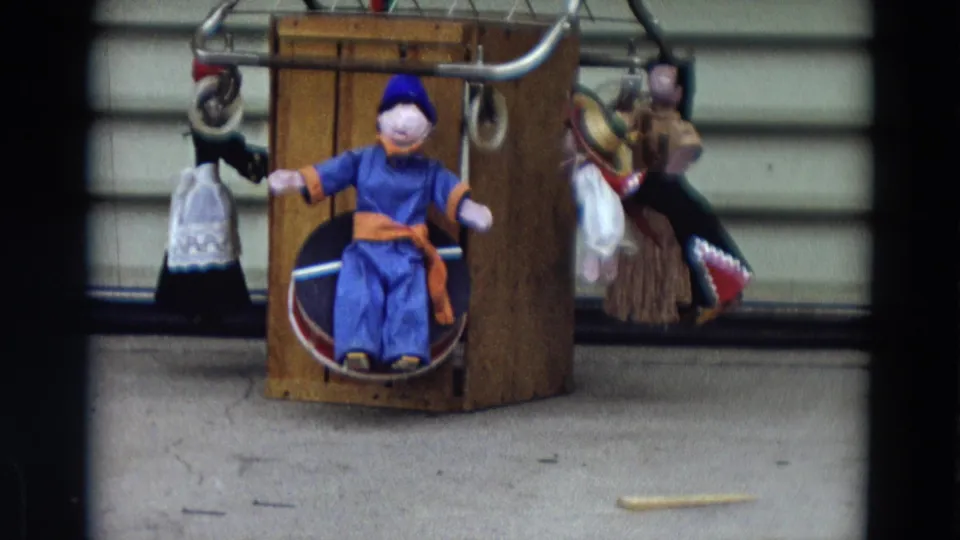 1968 Lahaina, Maui frame with a closer view of a blue-clothed seated doll and adjacent dressed dolls on a display stand.
