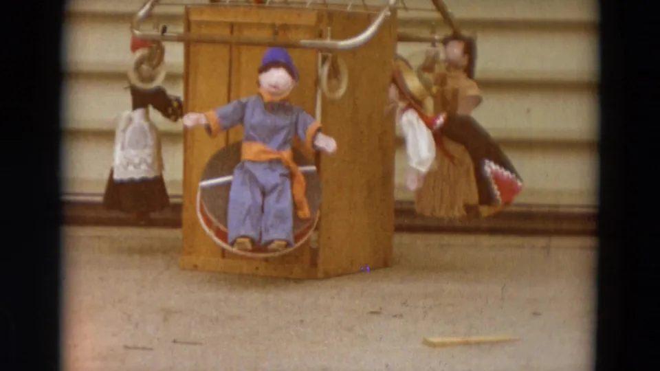 Warm-exposed 1968 Lahaina, Maui 8mm frame showing the same seated puppet display with visible grain and color shift.