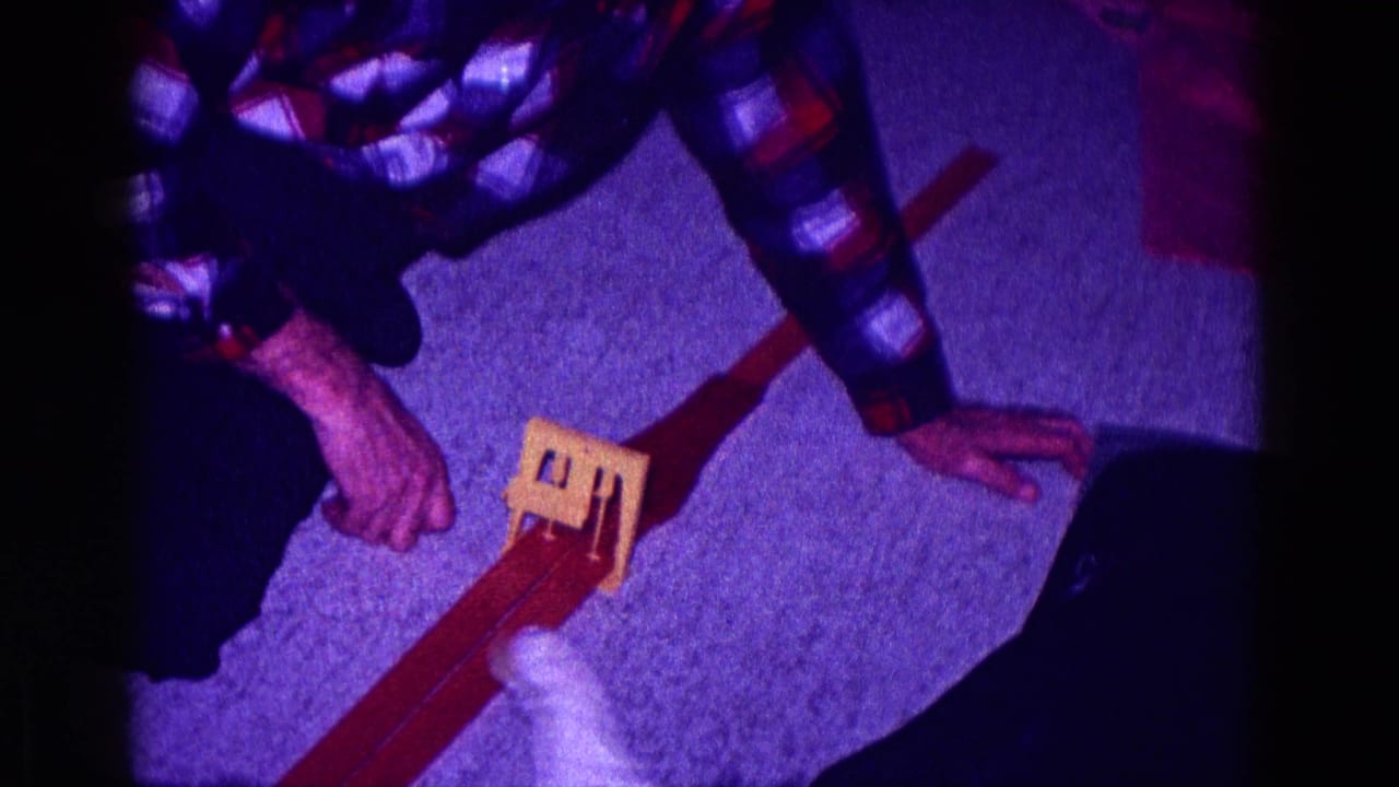 1968 Minnesota home-movie frame showing hands near fabric and a small wooden object on a carpeted private interior floor.