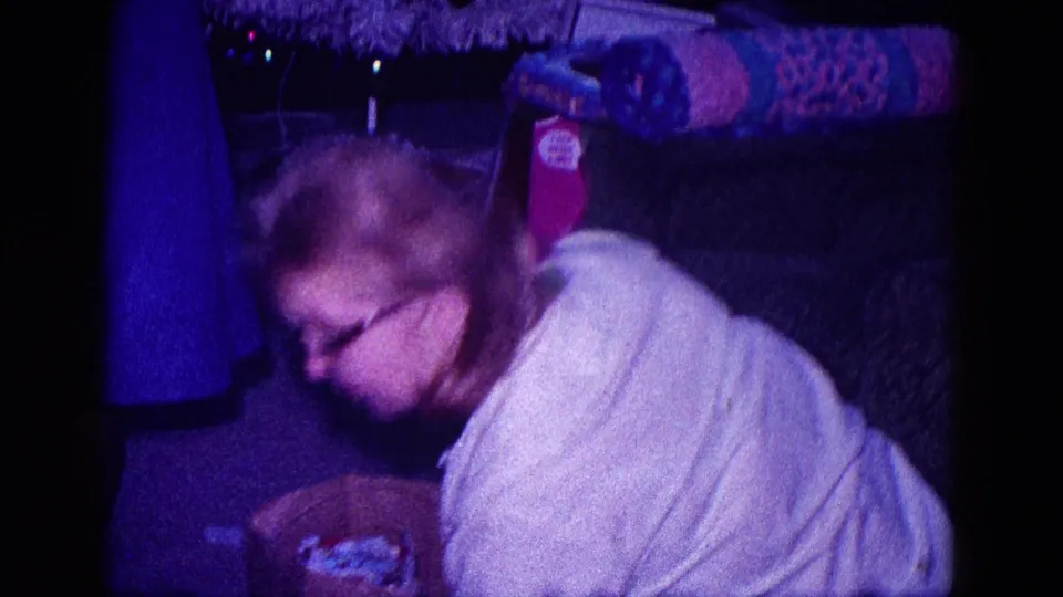 Motion-blurred 1968 Minnesota home-movie frame of a woman leaning over fabric or tools in a private carpeted room.