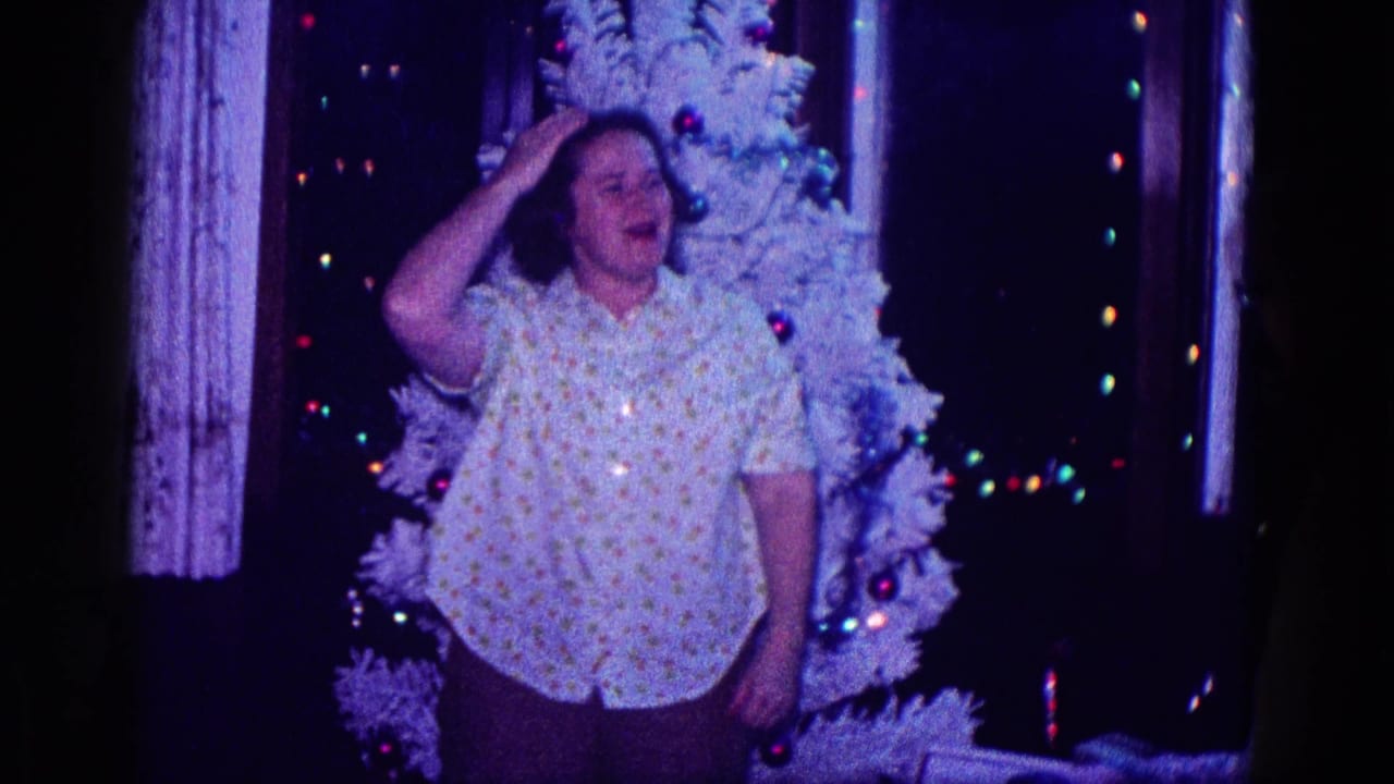 Woman standing before a white Christmas tree in a dim room with colored lights.