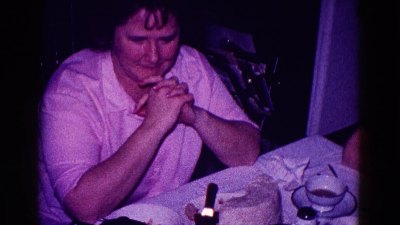 Woman with clasped hands seated at a dinner table with cups and dessert nearby.