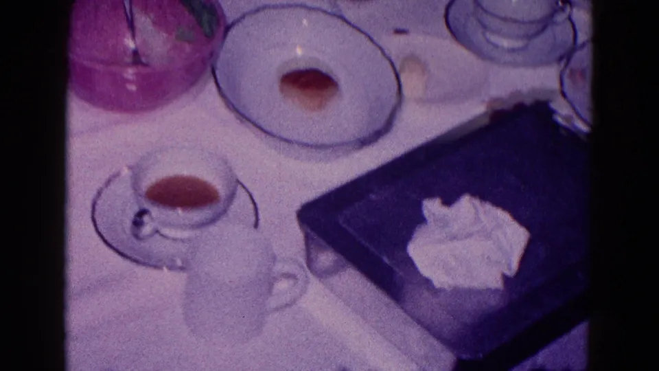 1968 Minnesota home-movie close-up of tea cups, saucers, a plate with cake or dessert, napkins, and a dark tray on a family table.