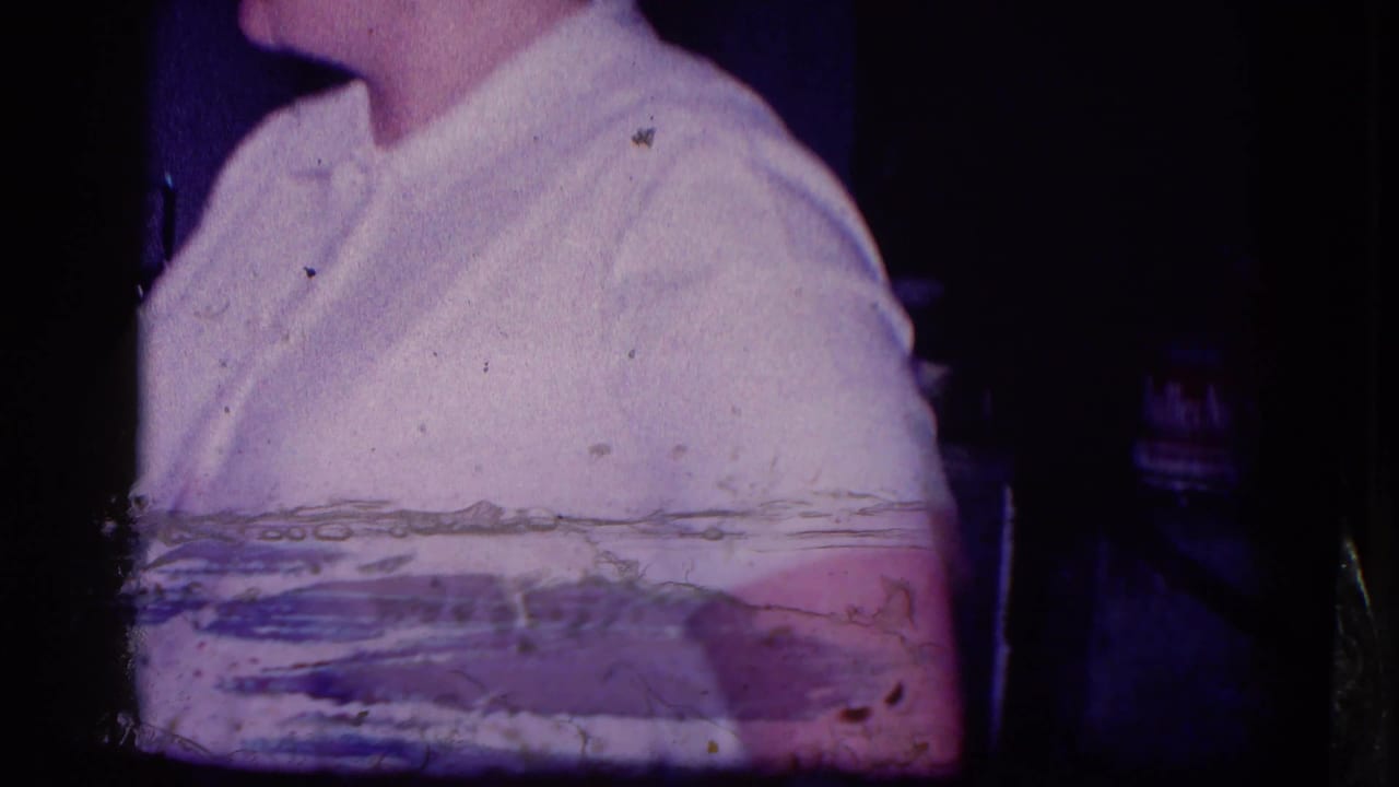 A partial adult figure in light clothing appears at the edge of a 1968 Minnesota home-movie frame, with film wear and dark borders visible.