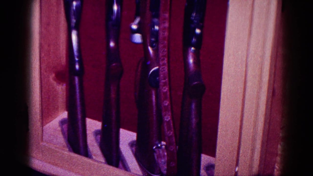 1968 Minnesota home-movie frame showing upright rifles in a light wood display cabinet with deep red lining.