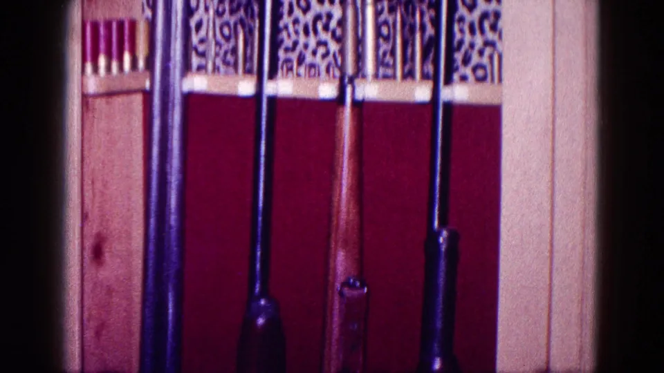 1968 Minnesota frame showing upright rifles in a red-lined wooden gun cabinet below decorative upper trim.