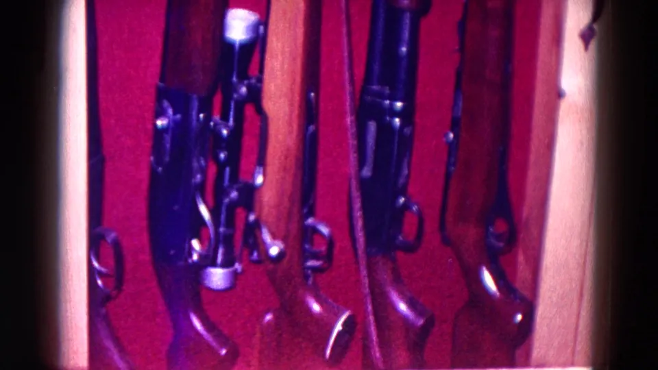 The final frame holds on a tighter view of rifle stocks, barrels, and hardware inside the 1968 Minnesota home display.